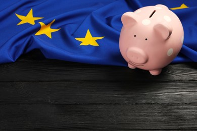 Pink piggy bank and flag of European Union on black wooden table. Space for text