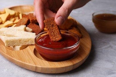 Photo of Woman dipping crispy rusk in sauce at light marble table, closeup