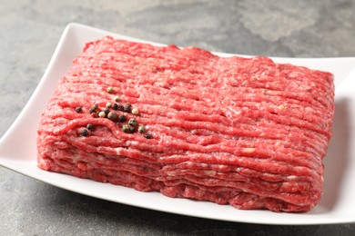 Raw ground meat and peppercorns on grey table, closeup