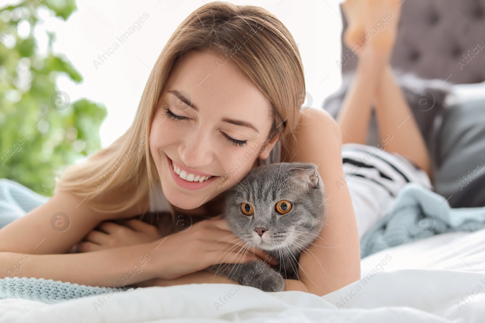 Photo of Young woman with her cute pet cat on bed at home