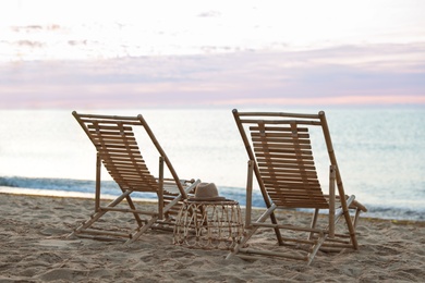 Photo of Wooden deck chairs and wicker table on sandy beach at sunset. Summer vacation