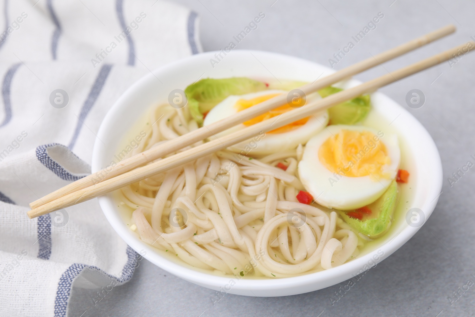 Photo of Bowl of delicious rice noodle soup with celery and egg on light grey table, closeup