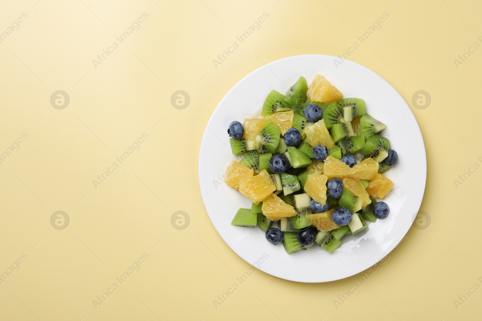 Photo of Plate of tasty fruit salad on pale yellow background, top view. Space for text