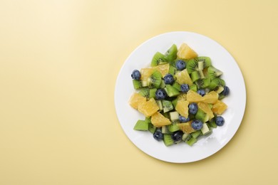 Plate of tasty fruit salad on pale yellow background, top view. Space for text