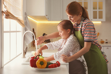 Mother and daughter washing vegetables in kitchen