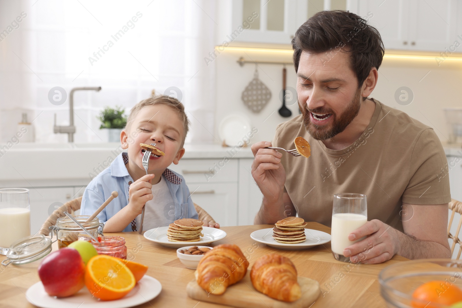 Photo of Father and his cute little son having breakfast at table in kitchen