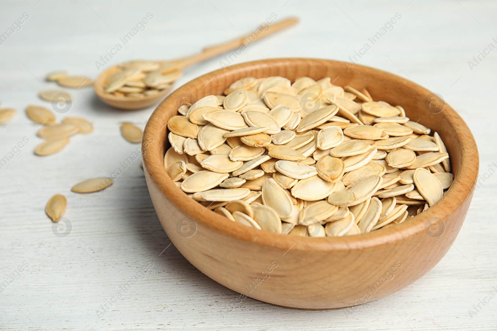 Photo of Bowl of raw pumpkin seeds on white wooden table