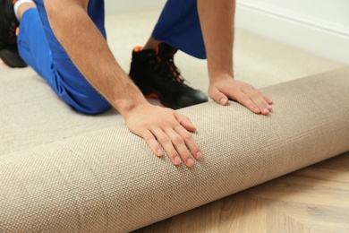 Photo of Worker rolling out new carpet flooring indoors, closeup