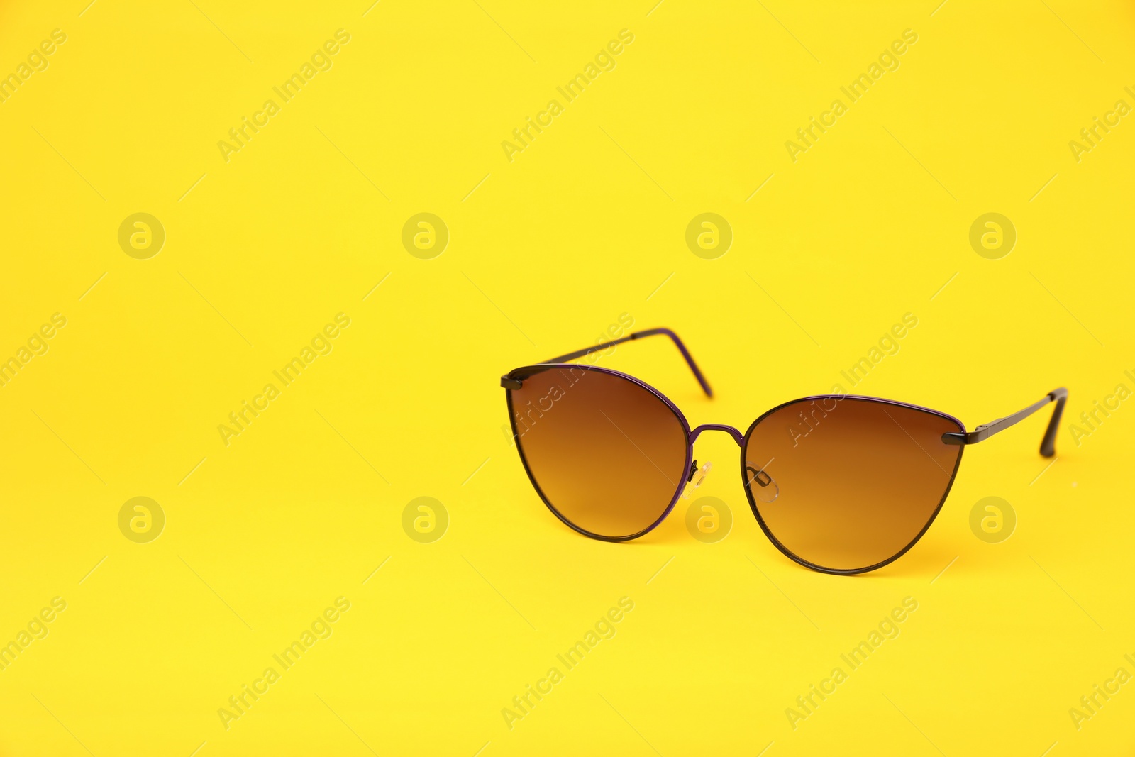 Photo of New stylish sunglasses on yellow background, space for text