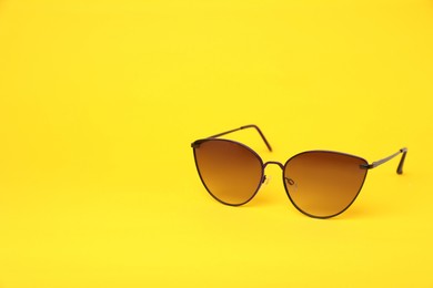 Photo of New stylish sunglasses on yellow background, space for text