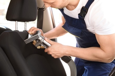Photo of Male worker removing dirt from car seat with professional vacuum cleaner