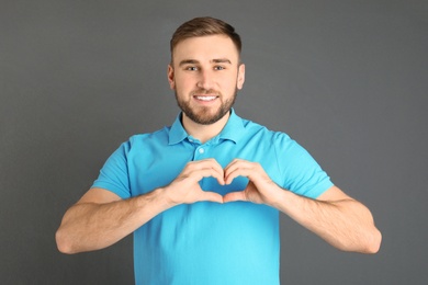 Photo of Young man making heart with his hands on grey background