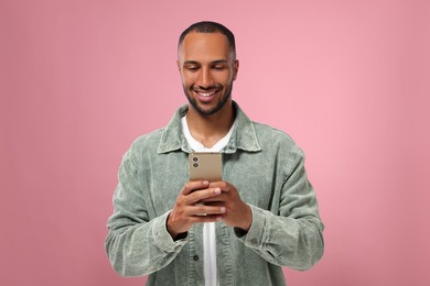 Photo of Happy man sending message via smartphone on pink background