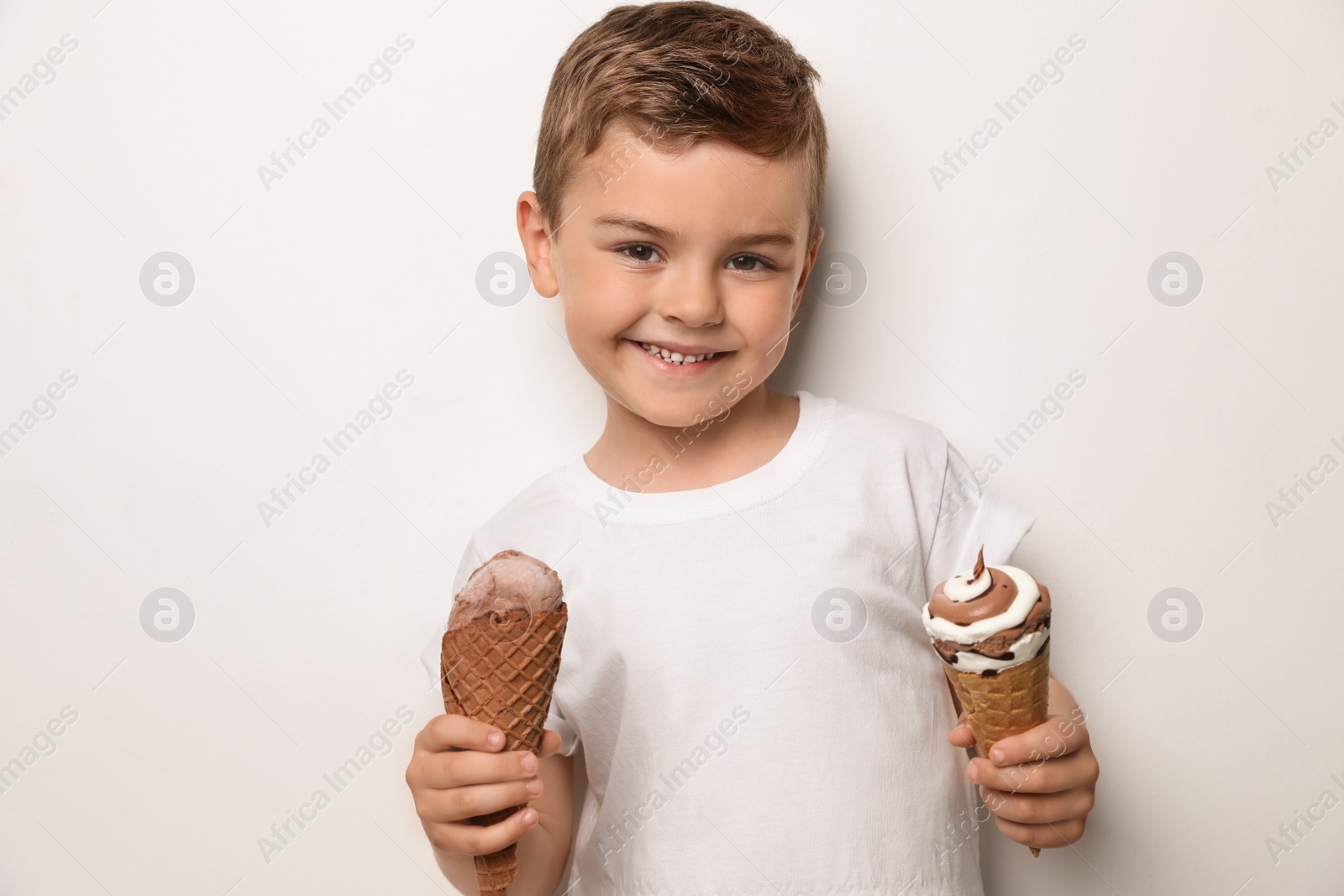 Photo of Adorable little boy with delicious ice creams against light background