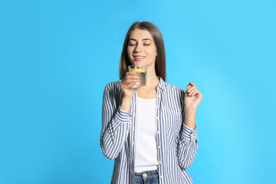 Photo of Young woman with glass of lemon water on light blue background