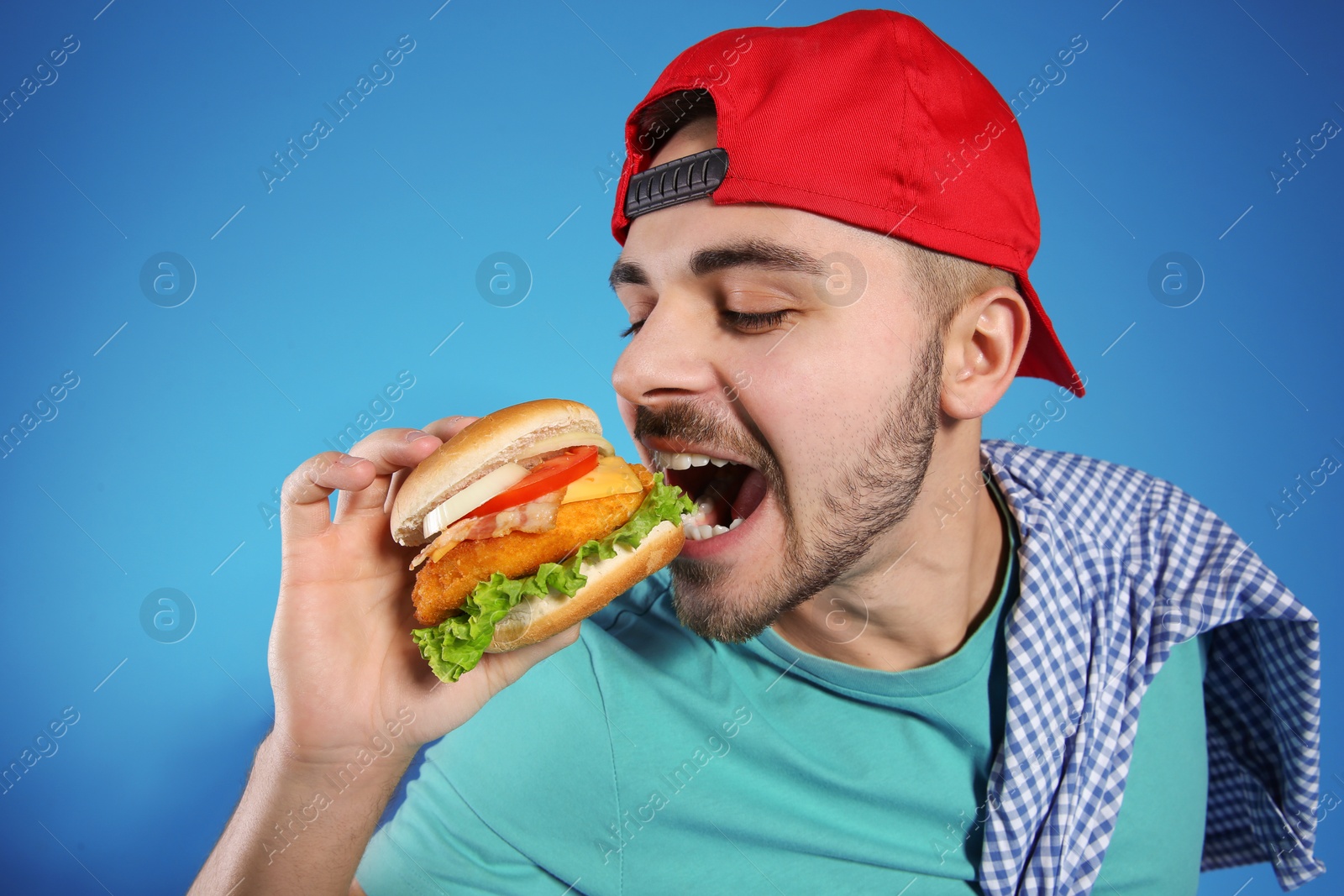 Photo of Handsome man eating tasty burger on color background