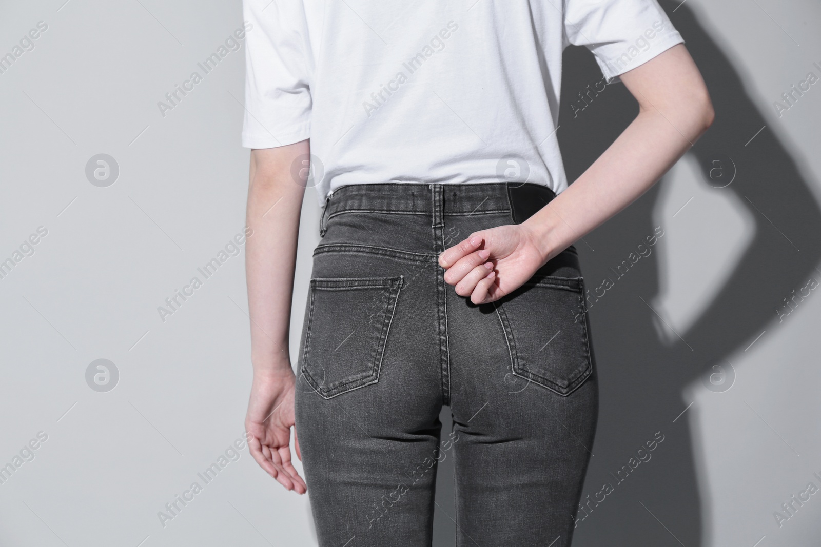 Photo of SOS gesture. Woman showing signal for help behind her back on light background, back view