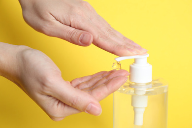 Woman applying antiseptic gel on hand against yellow background, closeup