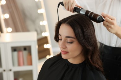 Hairdresser working with beautiful woman using curling hair iron in salon. Space for text