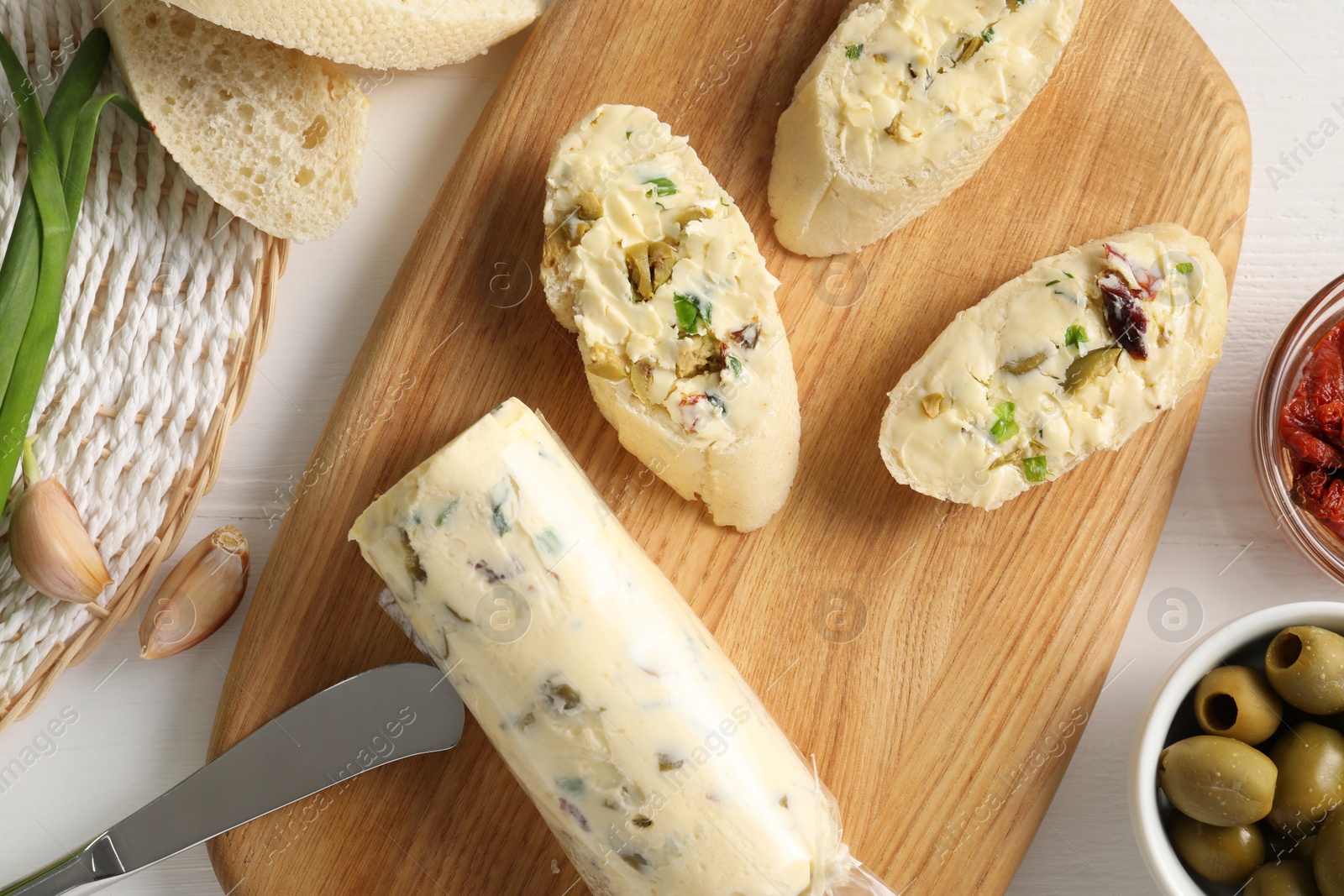 Photo of Tasty butter with green onion, olives, garlic and bread on white wooden table, top view