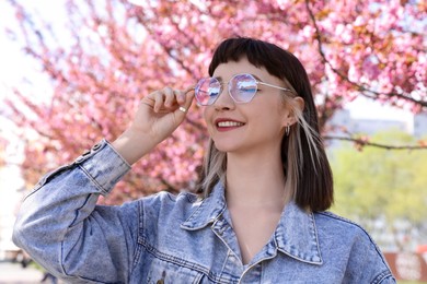 Photo of Beautiful young woman near blossoming sakura trees in park