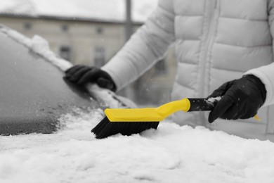 Photo of Man cleaning snow from car hood outdoors, closeup