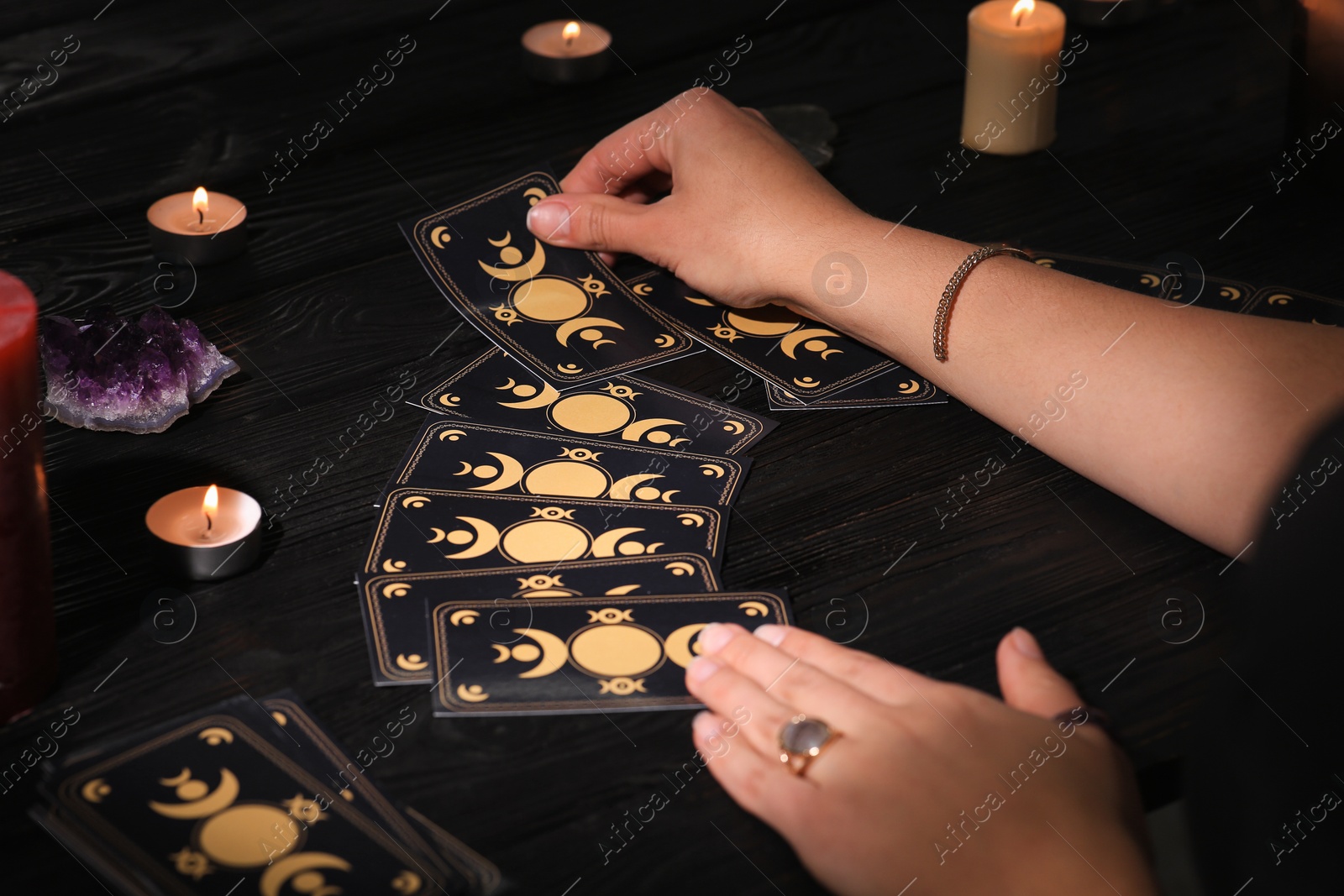 Photo of Soothsayer predicting future with tarot cards at table in darkness, closeup