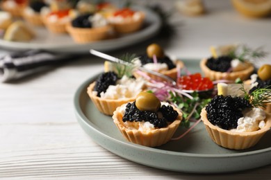 Delicious tartlets with caviar and cream cheese served on white wooden table, closeup