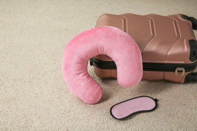 Photo of Pink travel pillow, suitcase and sleep mask on beige rug, space for text