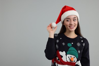 Photo of Happy young woman in Christmas sweater and Santa hat on grey background. Space for text