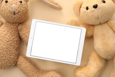 Photo of Modern tablet and stuffed animals on beige background, flat lay. Space for text