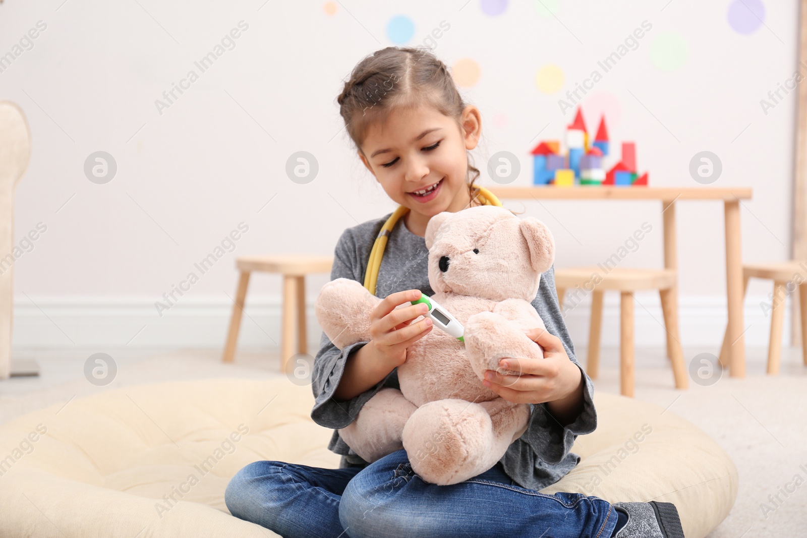 Photo of Cute child playing doctor with stuffed toy on floor in hospital