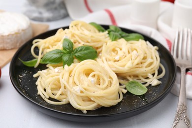 Photo of Delicious pasta with brie cheese and basil leaves on white table, closeup