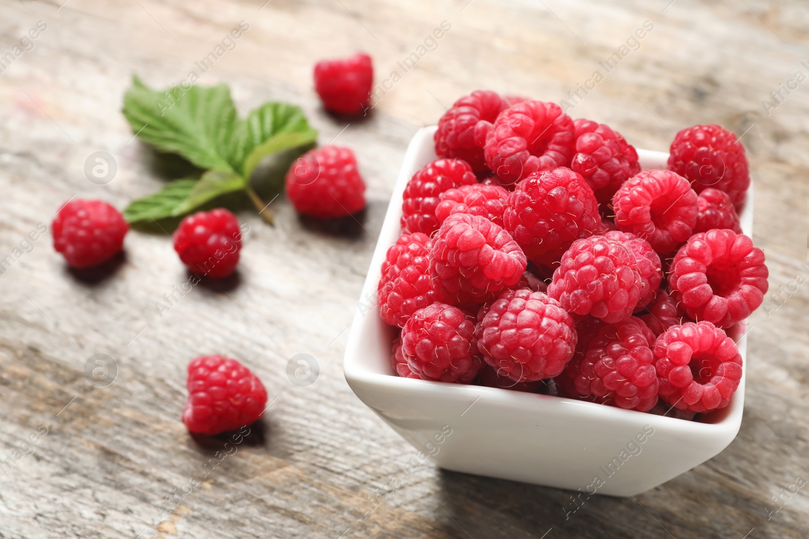 Photo of Bowl with ripe aromatic raspberries on wooden table