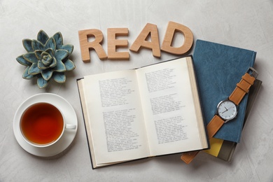 Flat lay composition with hardcover book and word READ made of wooden letters on grey background