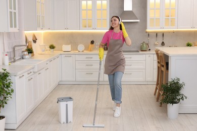 Photo of Enjoying cleaning. Happy woman in headphones listening music and mopping floor in kitchen