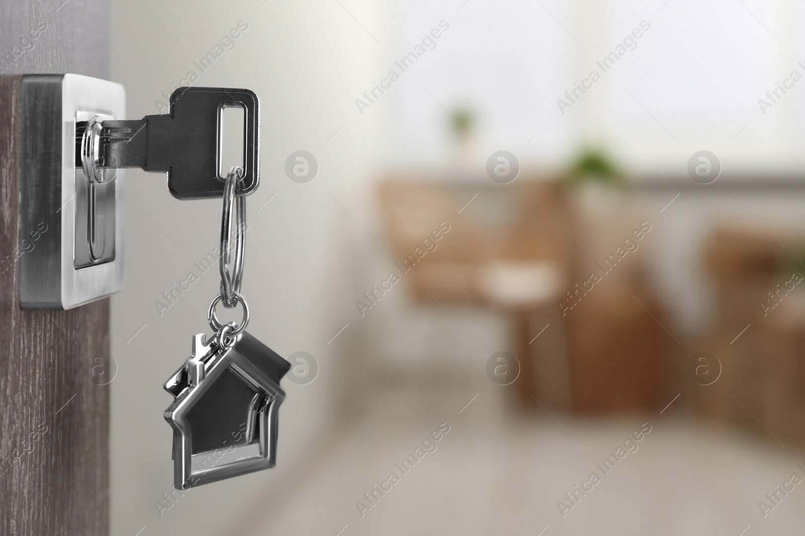 Photo of Mortgage and real estate. Open door with key and house shaped keychain against blurred background, space for text