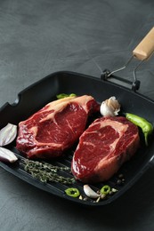 Grill pan with pieces of fresh beef meat, thyme and spices on gray table, space for text