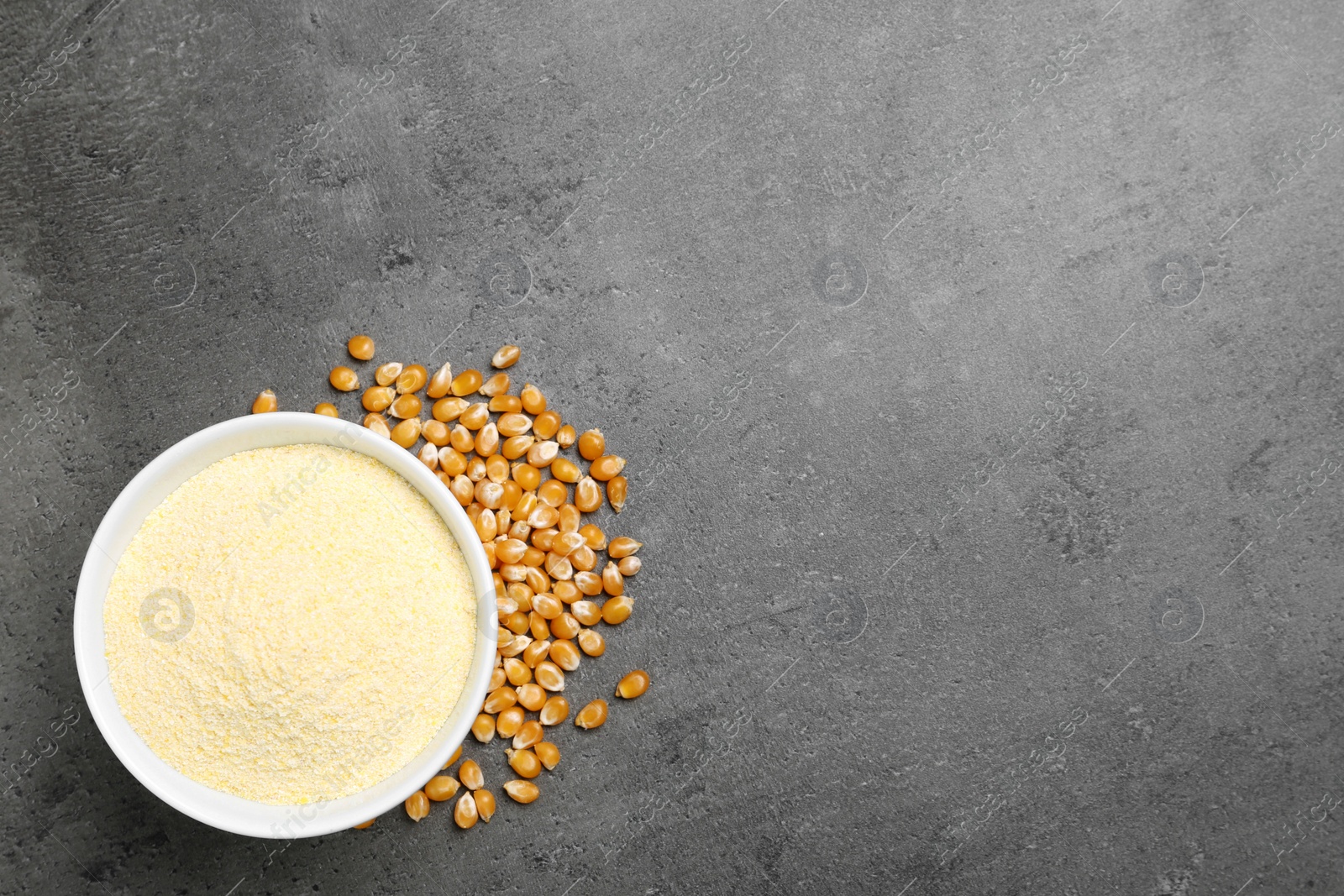 Photo of Bowl with corn flour and kernels on grey background, top view. Space for text