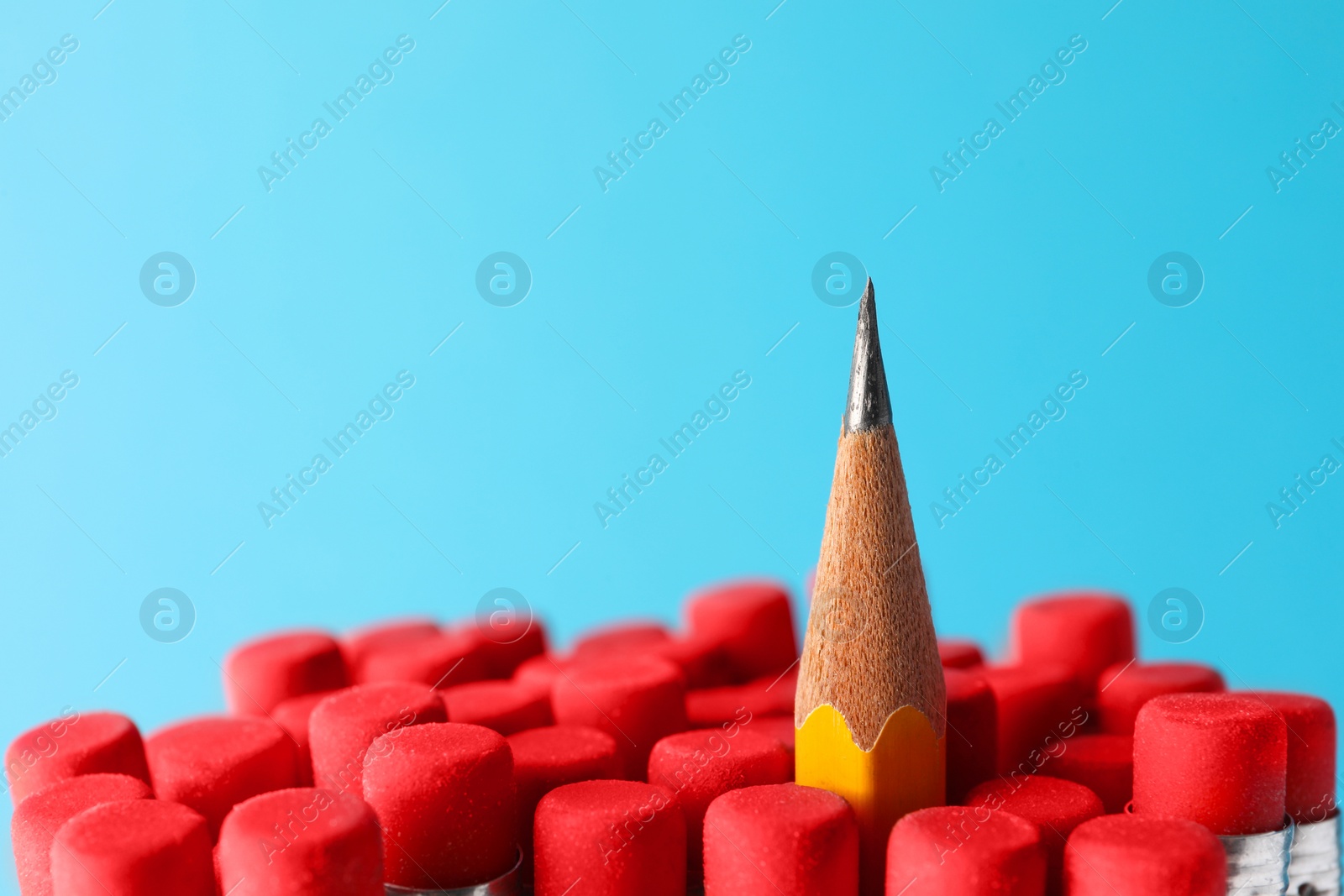 Photo of Sharp graphite pencil among others with erasers on light blue background, closeup. Space for text
