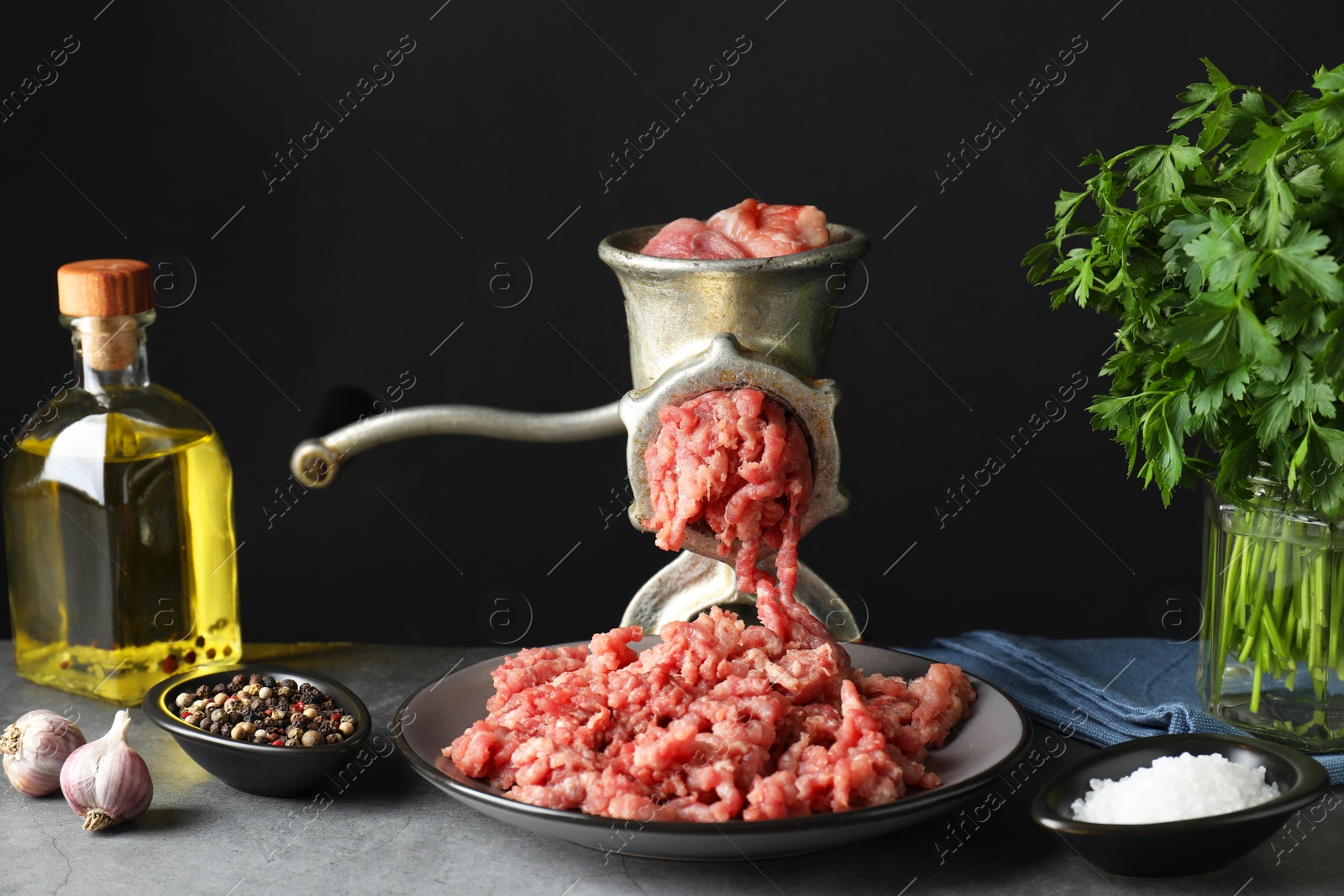 Photo of Manual meat grinder with beef mince, spices, oil and parsley on grey table