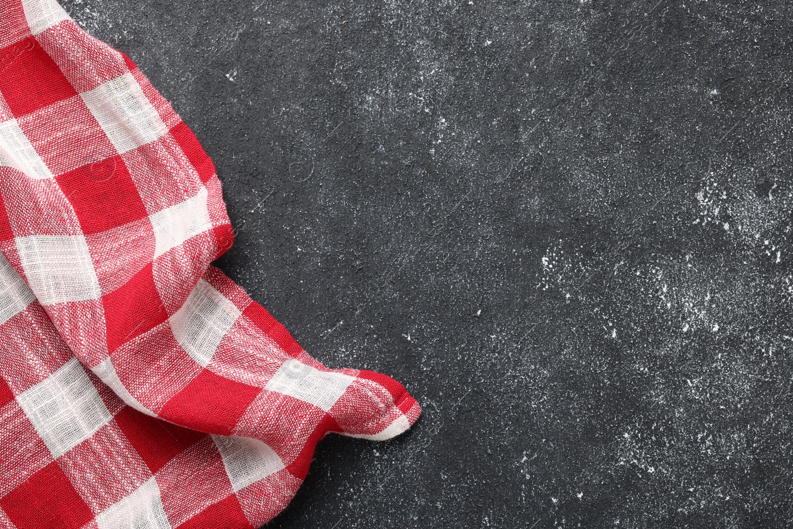 Photo of Red checkered tablecloth on black textured table, top view. Space for text