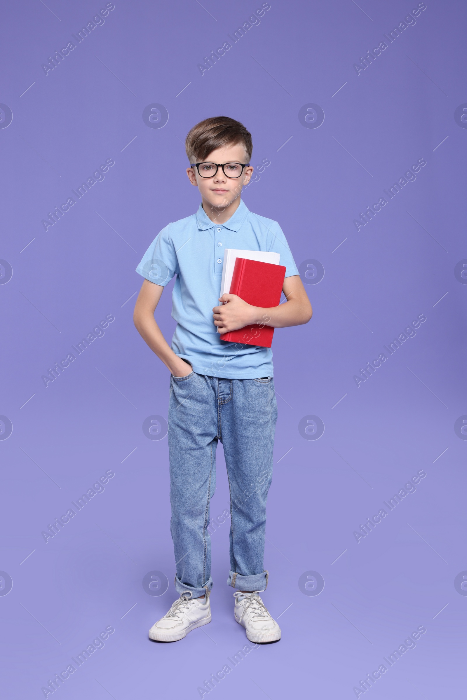 Photo of Cute schoolboy in glasses holding books on violet background