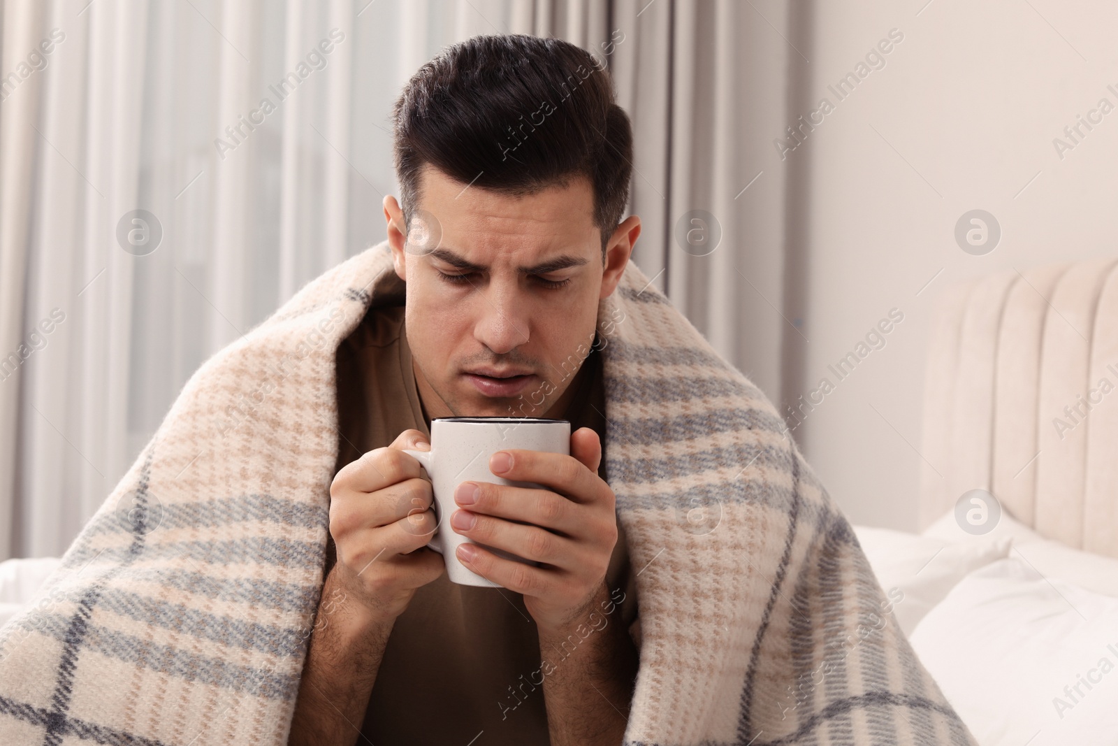 Photo of Sick man with cup of hot drink on bed at home