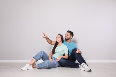 Photo of Young couple sitting on floor near light grey wall indoors