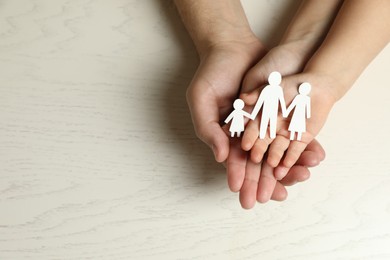 Father and child holding paper cutout of family at white wooden table, top view