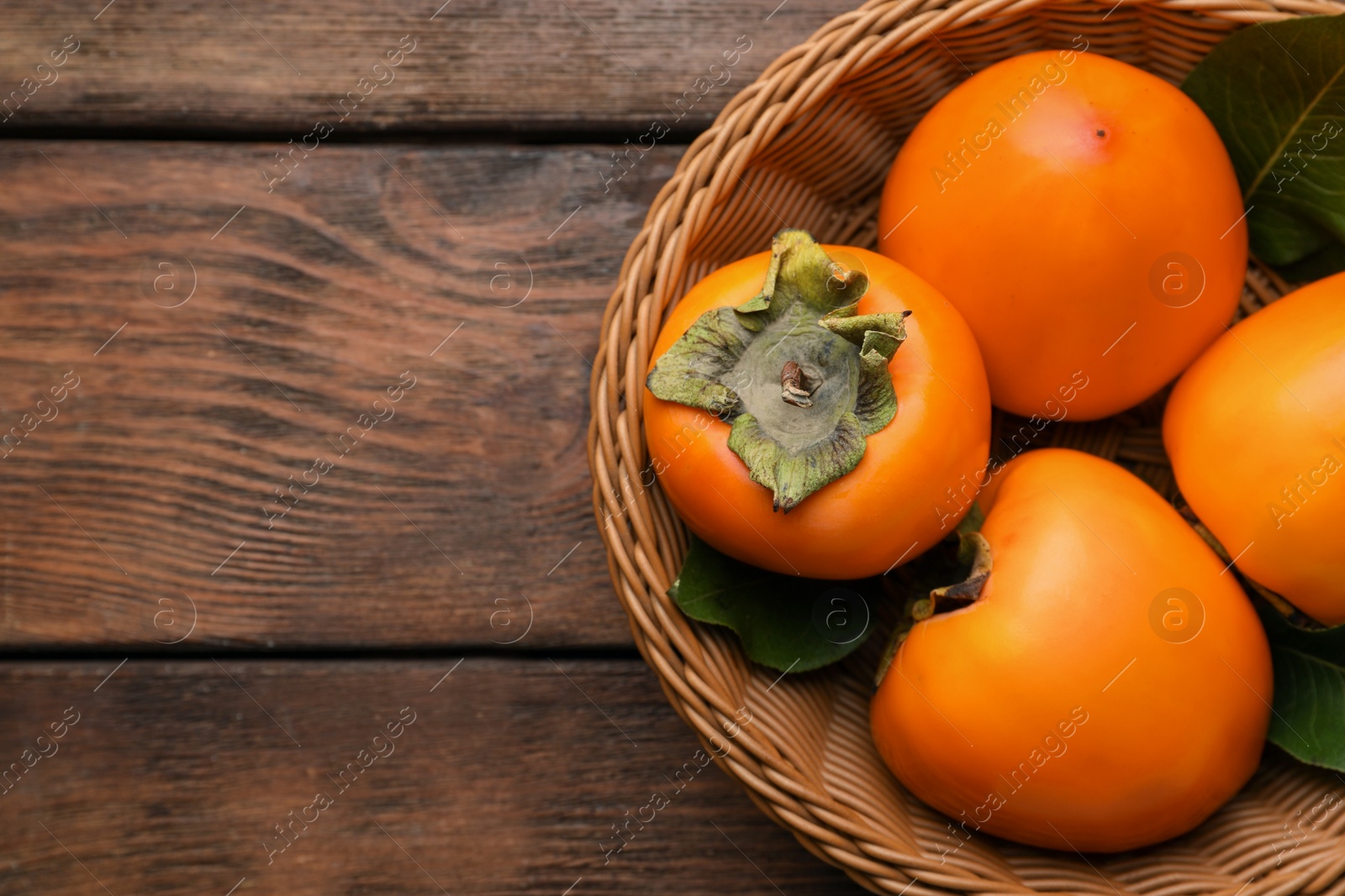 Photo of Delicious ripe persimmons in wicker basket on wooden table, top view. Space for text