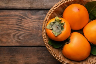 Delicious ripe persimmons in wicker basket on wooden table, top view. Space for text