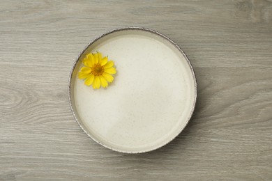 Photo of Beige bowl with water and yellow flower on wooden table, top view