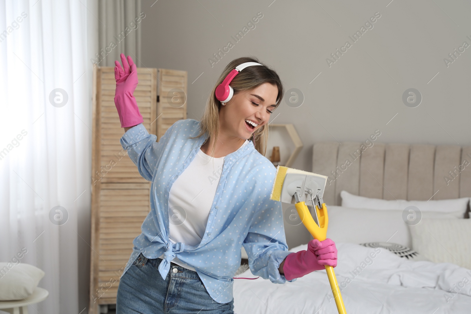 Photo of Woman in headphones with mop singing while cleaning at home